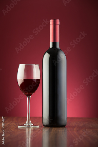 Bottle and glass full of red wine over a red backdrop