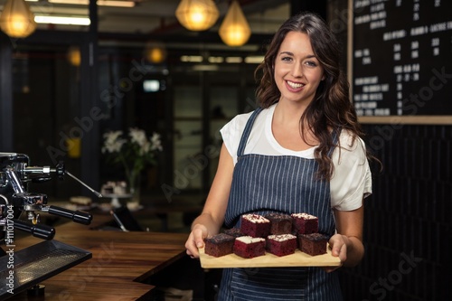 Smiling barista holding plate with cakes