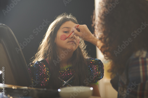 Mother painting daughter rosy cheeks for halloween