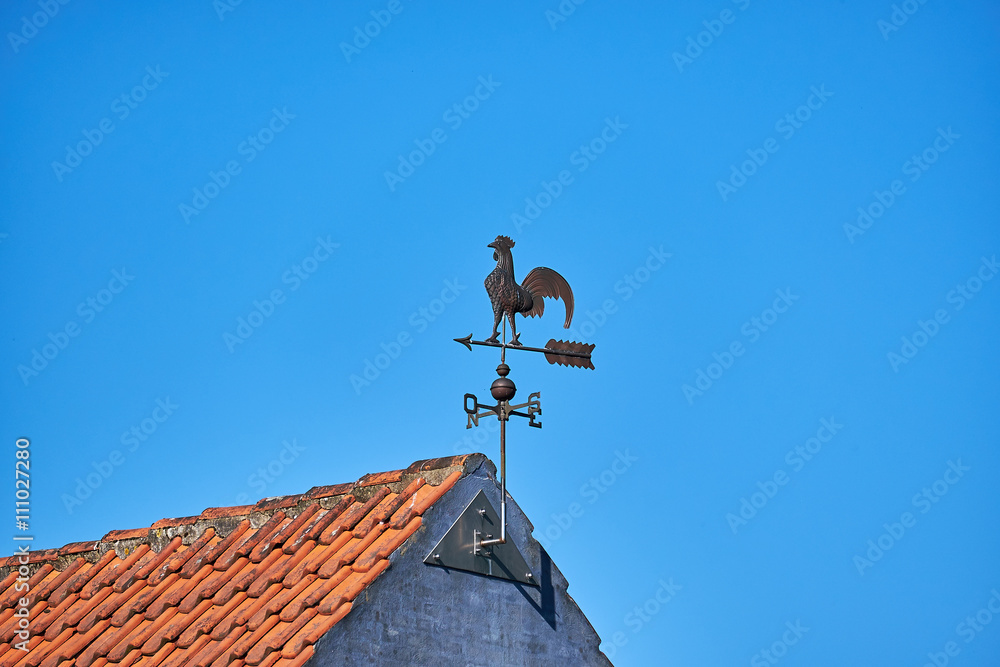 Metal weathervane attached to the gabe of masonry house with red roof tiles