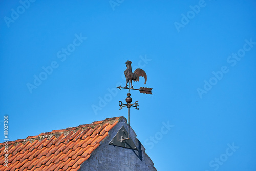 Metal weathervane attached to the gabe of masonry house with red roof tiles