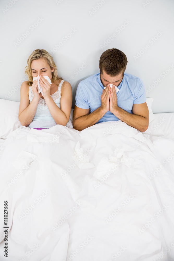 Couple covering nose while sneezing on bed Couple covering nose while sneezing on bed