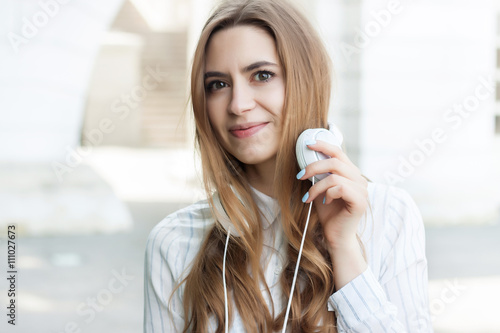 beautiful girl standing on the street with headphones and smilin photo