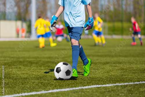 Young soccer player kicking ball in sports goalkeeper outfit © matimix
