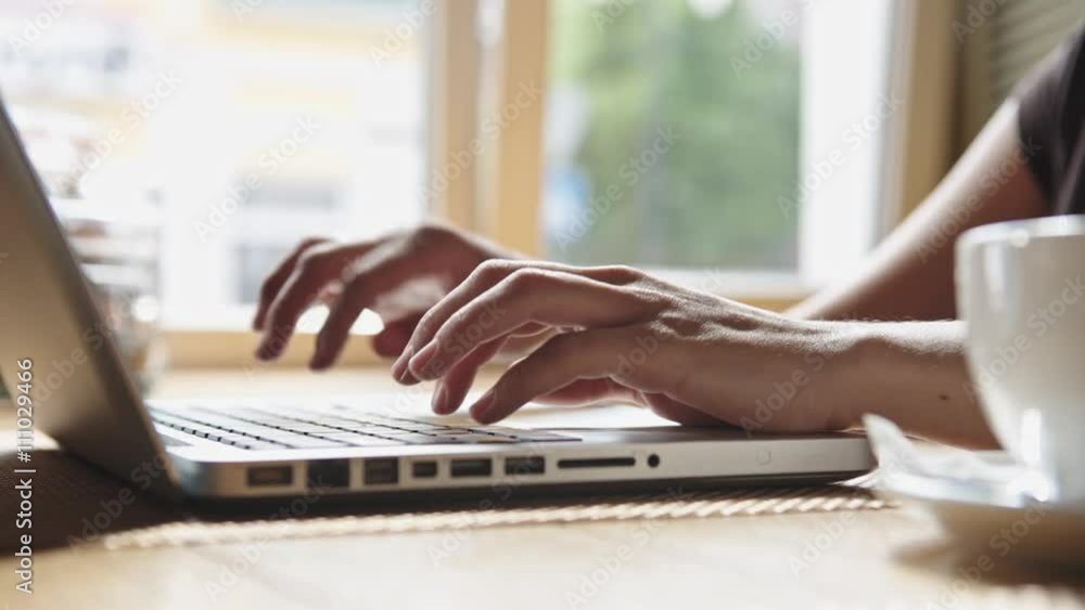 Woman working on laptop in the cafe near the window. Hands and fingers on the keyboard close-up Woman working on laptop in the cafe near the window. Hands and fingers on the keyboard close-up