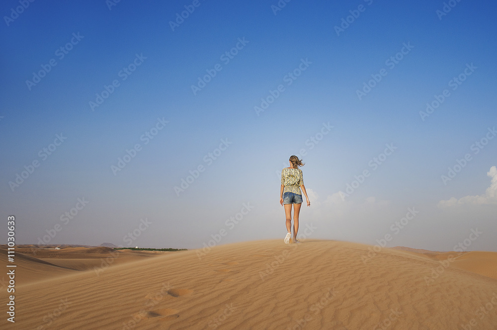 Young girl in denim shorts and a patterned blouse is walking alone on the sand dunes of the desert