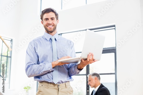 A businessman is holding his laptop and smiling