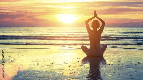 Woman practicing yoga at seashore during sunset.