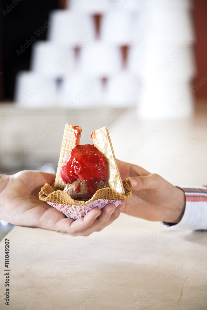 Waiter's Hand Serving Ice Cream With Strawberry Syrup To Woman
