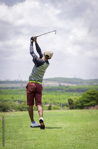 Golfer hitting golf shot with club on course while on summer vac