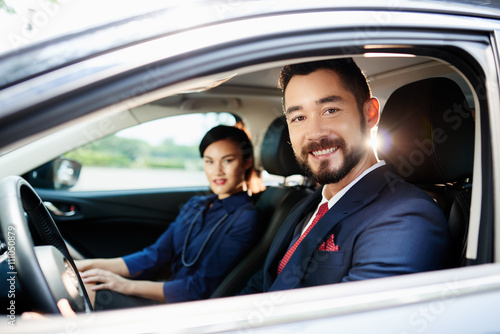 Cheerful young successful business couple driving car