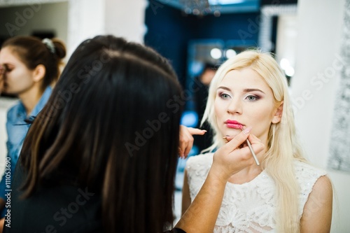 Young beautiful blonde bride applying wedding make up by makeup artist