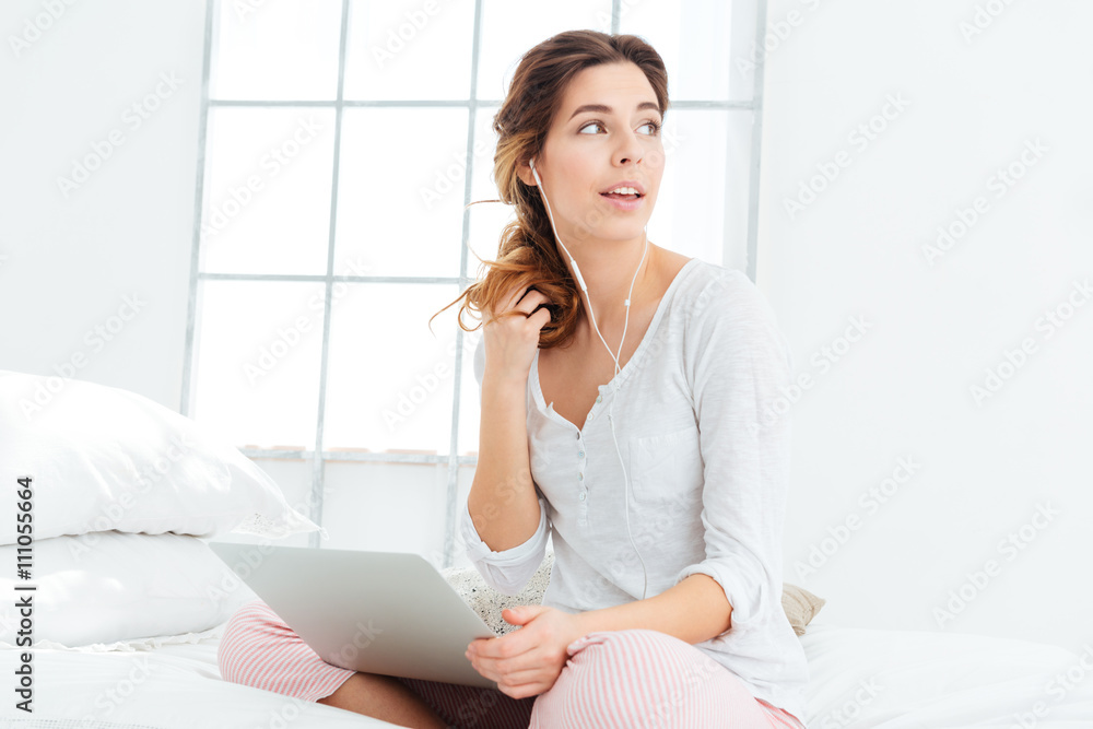 Woman sitting on the bed with laptop computer and headphones Woman sitting on the bed with laptop computer and headphones