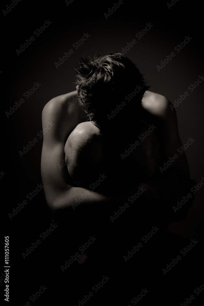 Naklejka premium Young Man Huddling on Floor Holding Knees to Chest