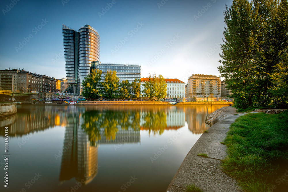 Vienna cityscape with modern Uniqa Tower on the water channel in the morning. Long exposure image technic with glossy water and reflection Vienna cityscape with modern Uniqa Tower on the water channel in the morning. Long exposure image technic with glossy water and reflection