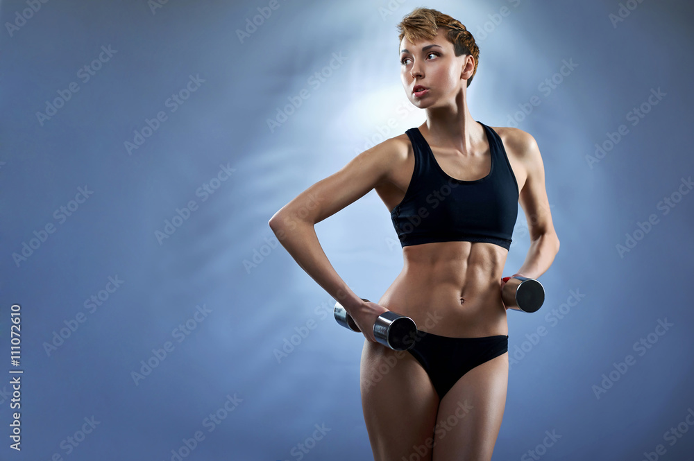 Fototapeta premium Healthy and strong. Studio shot of a young attractive fitness woman wearing black sportswear looking away holding dumbbells copyspace on the side on blue background