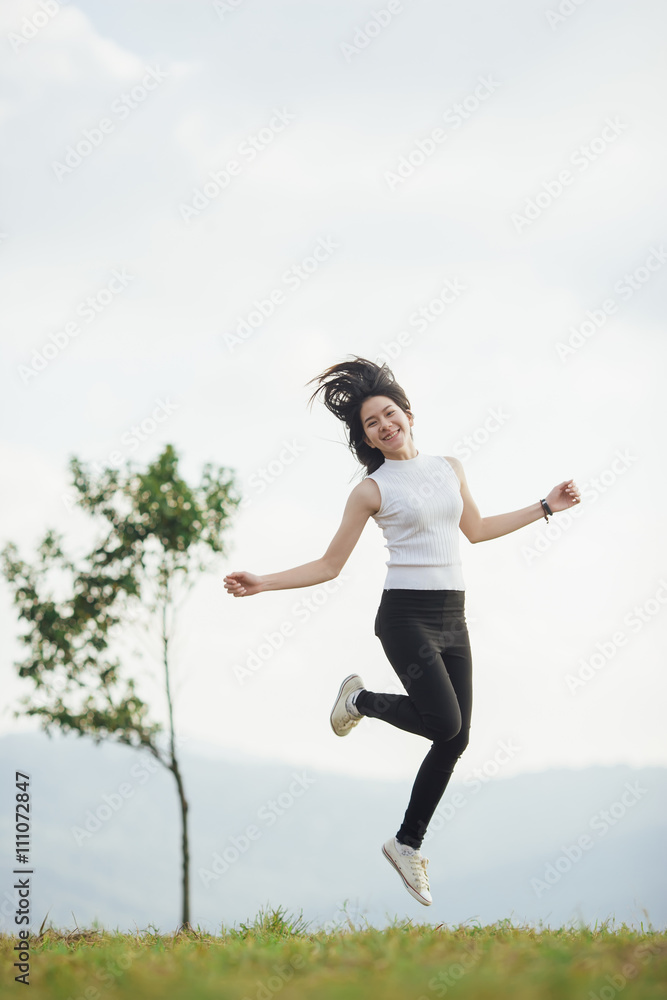 Happy jumping Asian girl on meadow.