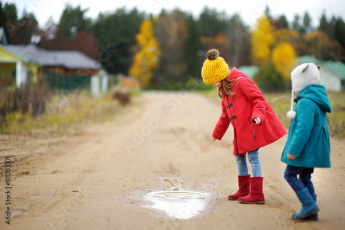 Two cute little sisters playing in a puddle on beautiful autumn day