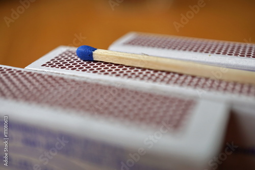 Safety match stick with a small blue head on the top of box of safety matches with its black striking surface with the honeycomb shapes on the narrower side 