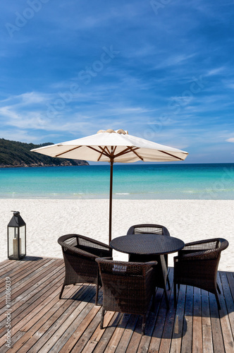 Rattan Stühle und Tisch unter Sonnenschirm auf Holzdeck am tropischen Strand
