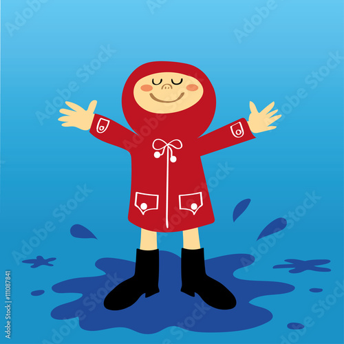 A small boy or girl in a red raincoat having fun splashing in the puddles after a shower of rain