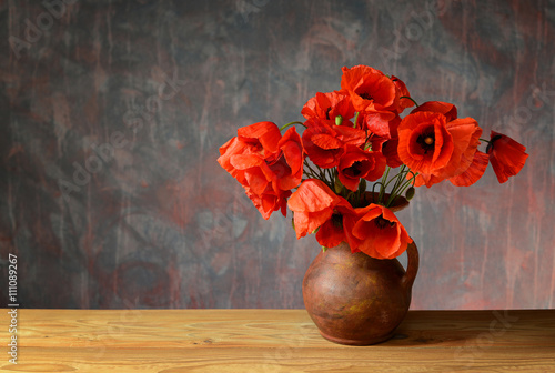 Red poppies in a ceramic vase on a wooden table