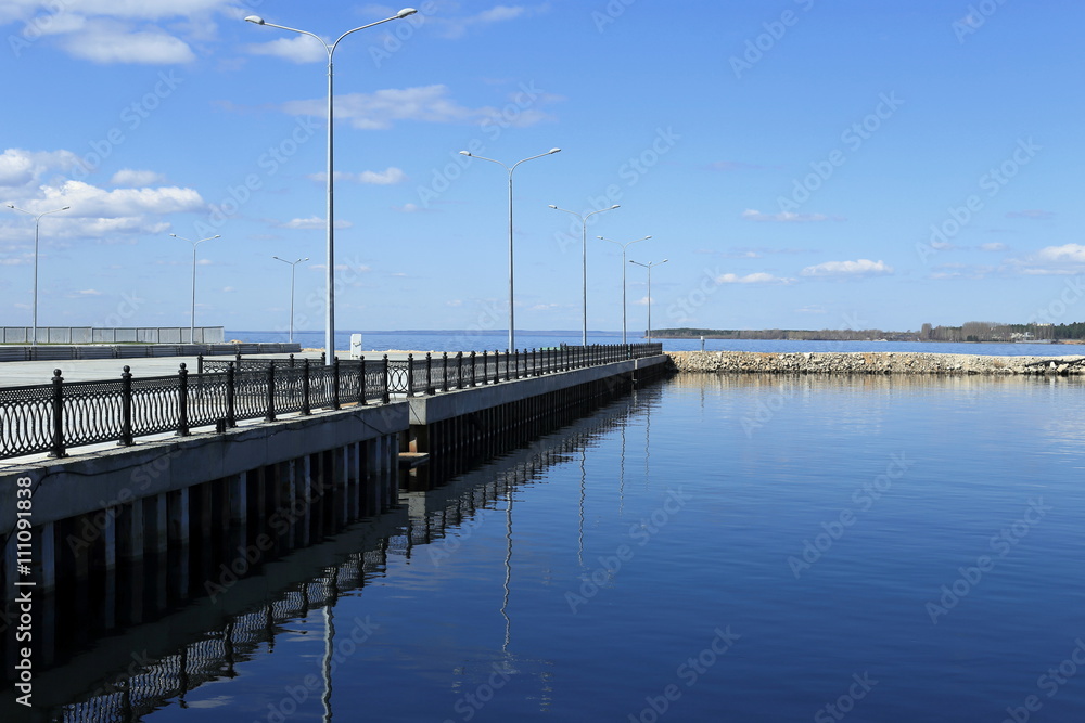 
empty pier and calm water on a background of blue sky and clouds. beautiful fencing and pillars.
