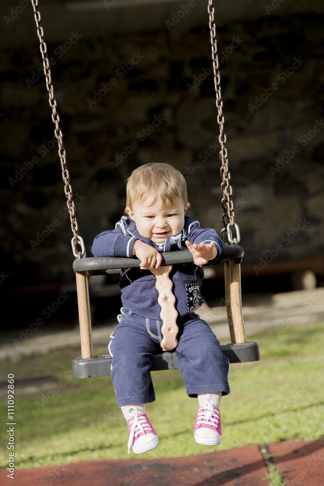Adorable baby on swing pulling her arm while looking down