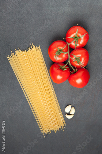 Pasta ingredients. Tomatoes, spaghetti pasta and garlic, on dark grunge backdrop, top view