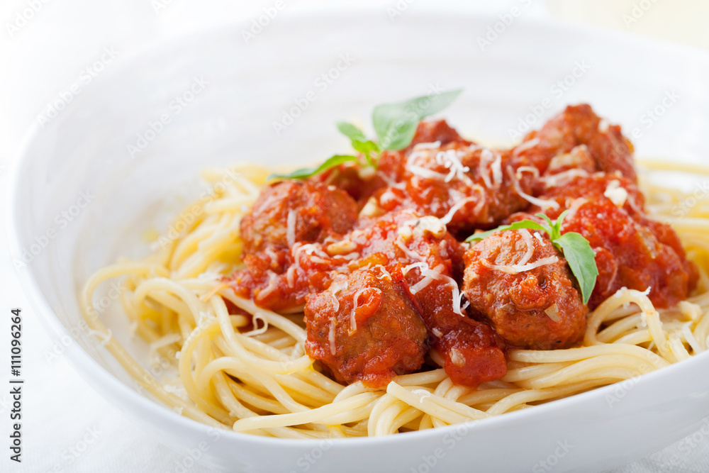 Meatballs in tomato sauce and fresh basil with spaghetti on a white plate