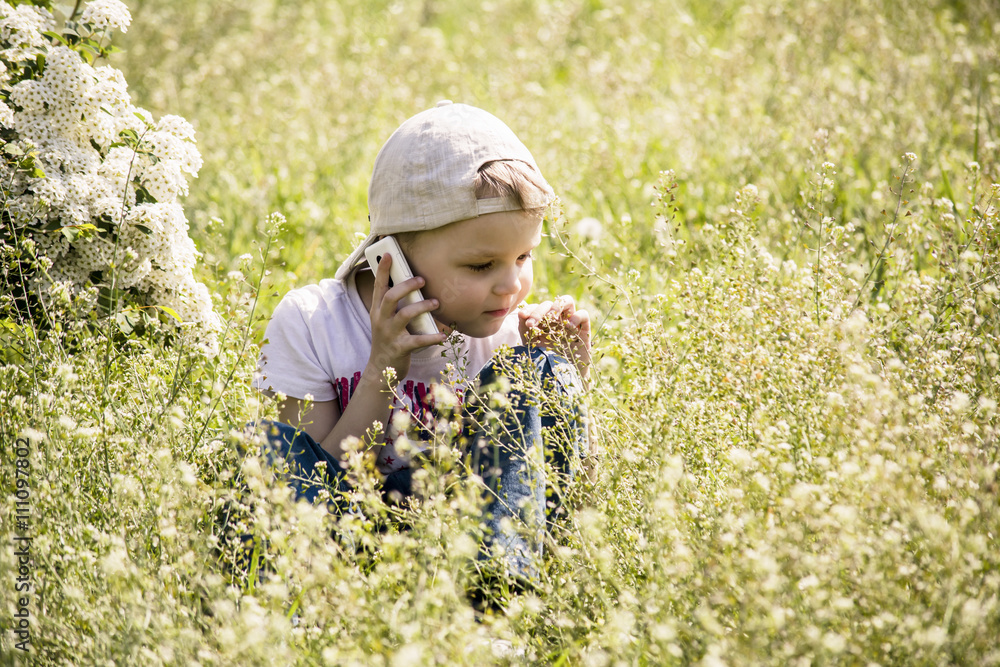 boy talking on a cell phone in the grass in the park boy talking on a cell phone in the grass in the park