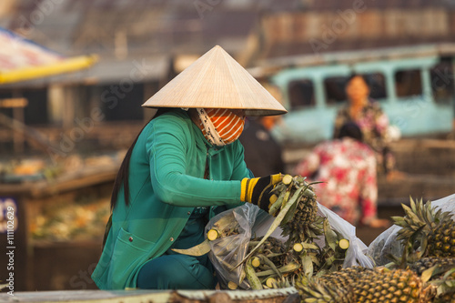 Vietnamese woman with typical conical hat ( sugegasa),  cut pineapple fruits in the  Cai Rang floating market on the Mekong delta. Can Tho, Vietnam