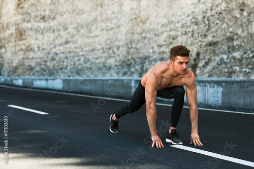 Sports. Healthy Athletic Man With Fit Muscular Body In Starting Position For Running On Road. Handsome Runner Ready To Start Sprint Race. Fitness Model Training Outdoors In Summer. Workout Concept