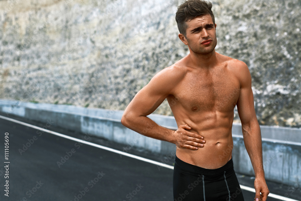 Obraz premium Stomach Ache. Closeup Portrait Of Athletic Man With Fit Muscular Body Touching Belly, Suffering From Abdominal Pain. Handsome Fitness Runner Feeling Bad After Running Outdoors. Sport Injury Concept