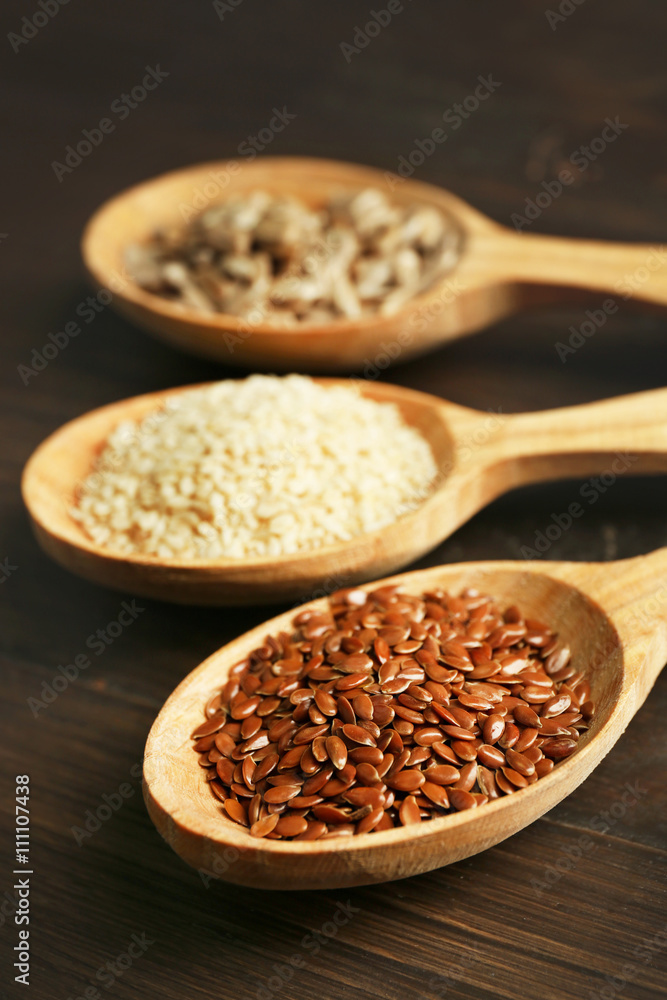Sesame, flax and sunflower seeds in wooden spoons on table, closeup Sesame, flax and sunflower seeds in wooden spoons on table, closeup