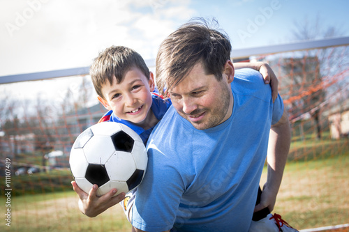 man with with child playing football on football pitch