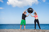 Sport und Fitness Instruktor zeigt junger Frau wie man mit Gymnastikball trainiert am Strand im Freien