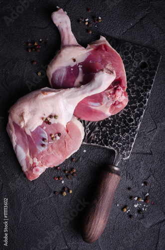 Raw duck legs with spices and large cutting chefs knife on dark slate background. Top view
