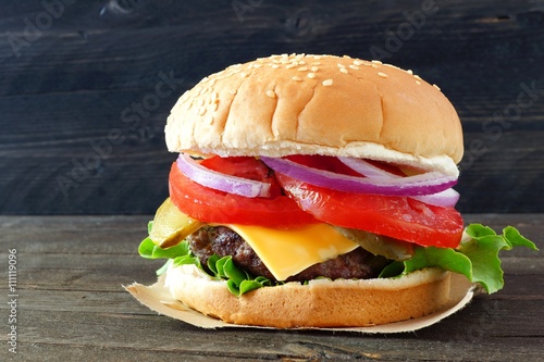 Classic hamburger with onions, tomato, cheese and lettuce on sesame seed bun over a dark wood background