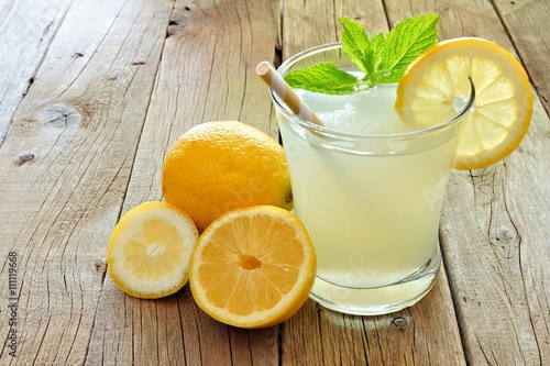 Glass of cold lemonade with lemon slices and mint on a rustic wood background