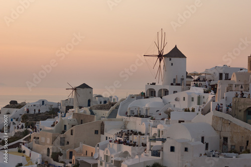 Sunset over white windmills in town of Oia and panorama to Santorini island, Thira, Cyclades, Greece