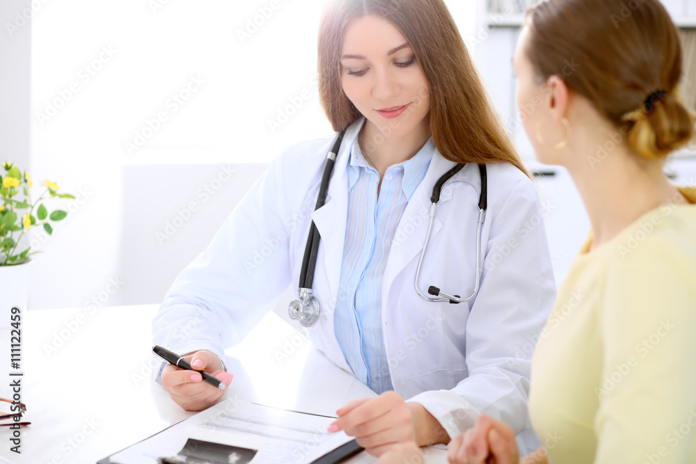 Doctor and patient sitting at the desk near window, sun shines Doctor and patient sitting at the desk near window, sun shines