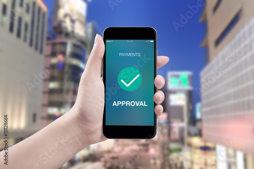 Hand holding mobile smart phone with payment approved screen on city background