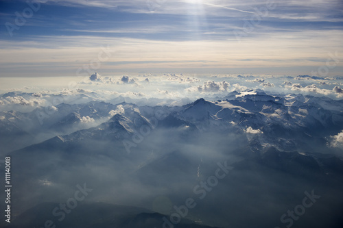 High altitude view of sunset over the mountains. Rays of light shine through the hazy atmosphere.
