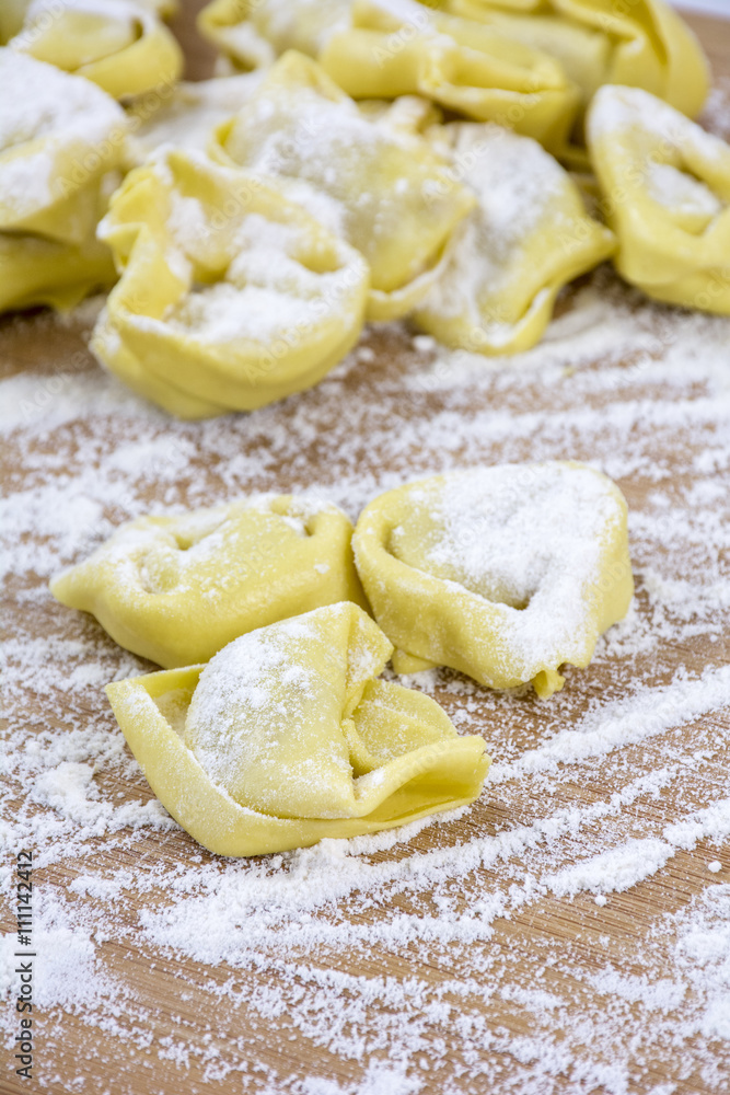 Several yellow ravioli on the wooden table with flour