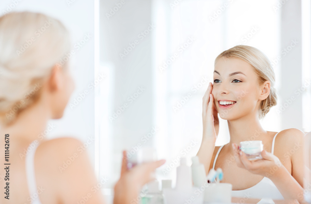 happy woman applying cream to face at bathroom happy woman applying cream to face at bathroom