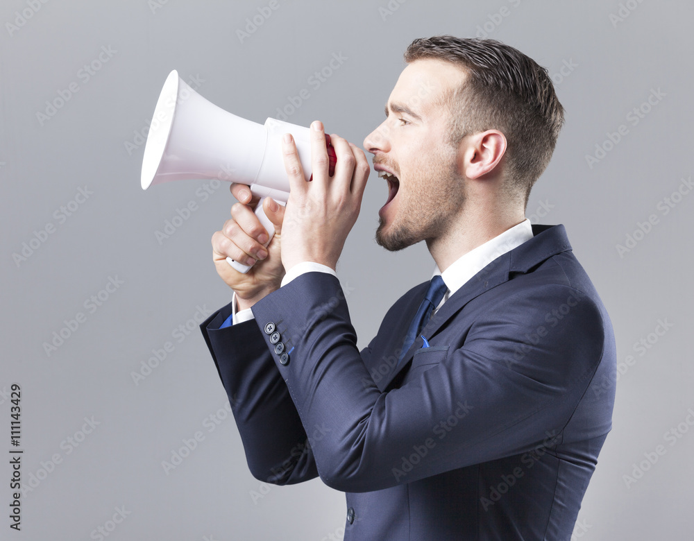 Handsome businessman shouting by megaphone on grey background Handsome businessman shouting by megaphone on grey background