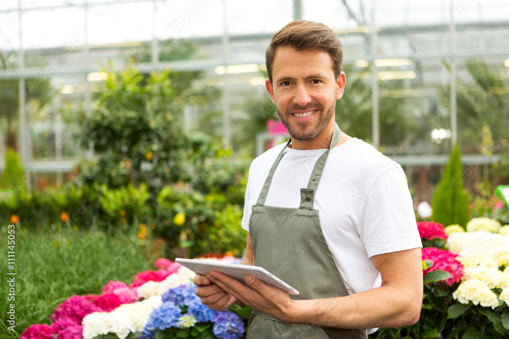 Young attractive man working at the plants nursery using tablet Young attractive man working at the plants nursery using tablet