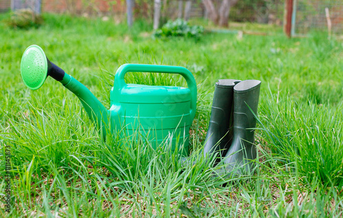 Rubber boots with watering can on grass