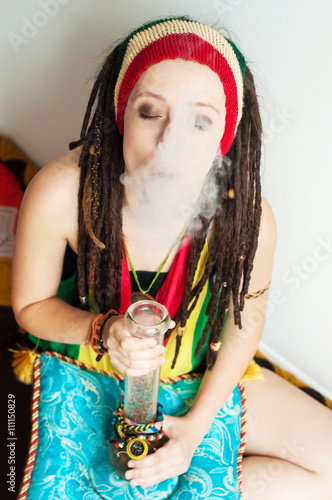 A young girl, dreadlock Rasta and Rasta hat, smokes drugs throug photo